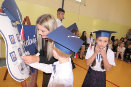Kobieta i dwójka uczniów przy symbolicznej szkolnej tarczy 