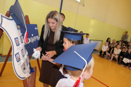 Kobieta i uczniowie przy symbolicznej szkolnej tarczy