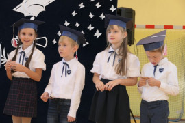 Czterej uczniowie w granatowych biretach na głowie stoją obok siebie