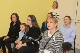 Grupa kobiet. Kobiety siedzą na ławce. Na kolanach jednej z nich siedzi dziecko 
