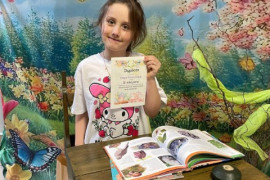 Dziewczynka siedzi za stolikiem w ręku trzyma dyplom 