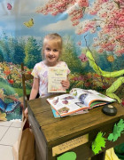 Dziewczynka siedzi za stolikiem w ręku trzyma dyplom 