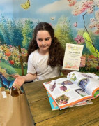 Dziewczynka siedzi za stolikiem. W ręku trzyma dyplom 