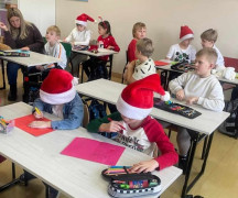 Dzieci siedzą w ławkach i przygotowują kartki świąteczne 