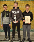 Trzej chłopcy stoją obok siebie. Jeden z nich trzyma w ręku dyplom 