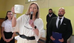 Kobieta trzyma w ręku kubek. Obok stoi mężczyzna 