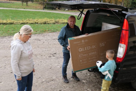 Kobieta, mężczyzna i mały chłopiec.  Mężczyzna wyciąga z bagażnika samochodu duże pudełko 