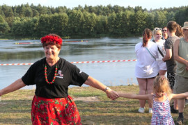 Uśmiechnięta kobieta w czerwonym wianku na głowie. Kobieta trzyma za rękę małą dziewczynkę 