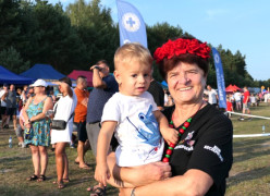 Kobieta w czerwonym wianku na głowie. Kobieta trzyma na ręku małego chłopca 