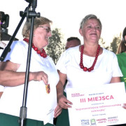 Dwie kobiety na scenie. Jedna z nich trzyma w ręku tabliczkę z czerwonymi napisami 
